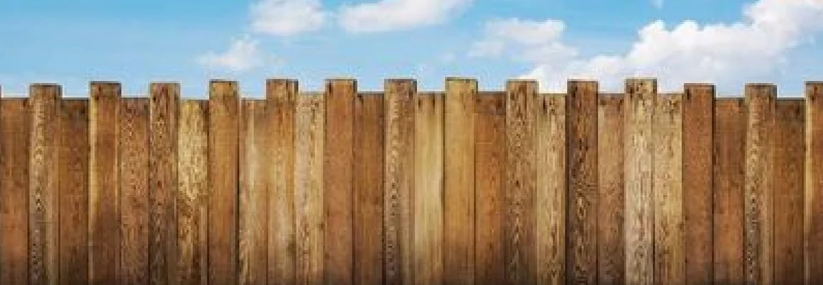 Ein Holzzaun vor blauem Himmel und grünem Rasen.